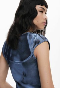 Blue, short-sleeved top with a soft texture. Back features a smooth, fitted design, showcasing a subtle sheen. No visible patterns or accents.