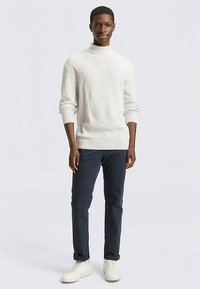 Lichtbeige geribbelde coltrui, gecombineerd met donkerblauwe broek en witte sneakers. Eenvoudig, aansluitend ontwerp met een textuurrijke afwerking.