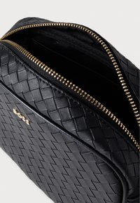 Czarna skórzana torebka o plecionym wzorze, z złotym zamkiem błyskawicznym i logo marki. Wnętrze wyłożone gładką podszewką, bez widocznych kieszeni.