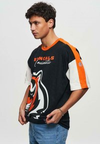 Musta ja oranssi NFL Cincinnati Bengals T-paita, jossa on suuri tiikerigrafiikka, lyhyet hihat kontrastivalkoisena ja logoyksityiskohtia.