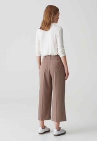 Lichtgekleurde sweater en bruine cropped broek met een brede pijp. Glad stoffen textuur. Draagt met witte sneakers. Eenvoudig ontwerp aan de achterkant.