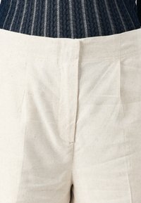 Lichtgekleurde linnen shorts met een zachte textuur, voorzien van een voorplooi en een op maat gemaakte tailleband, gecombineerd met een donker gebreid topje.