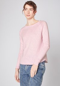 Helles rosa Langarmhemd aus einem weichen, strukturierten Stoff. Entspannte Passform mit Rundhalsausschnitt und leicht abgerundetem Saum. Getragen mit blauen Jeans.