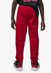 Pantalones de chándal rojos de forro polar con cintura elástica, piernas ajustadas y bolsillos laterales. Llevados con zapatillas negras y rojas con suelas blancas.