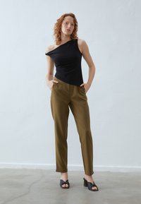 Crni top s jednim ramenom, maslinaste krojene hlače s prednjim džepovima i crne sandale s visokom petom. Glatka tkanina, prilagođen dizajn, elegantna silueta.