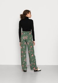 Top preto de gola alta emparelhado com calças largas florais verdes apresentando flores rosas e azuis e uma cintura elástica. Sapatos pretos.