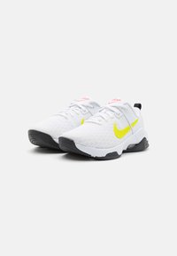Zapatillas deportivas blancas con parte superior de malla texturizada, Swoosh amarillo, acentos rosas y suela negra. Diseñadas para ofrecer comodidad y soporte en deportes.