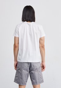 Weißes Baumwoll-T-Shirt mit kurzen Ärmeln, von hinten betrachtet, kombiniert mit grauen Cargo-Shorts, die über mehrere Taschen verfügen.