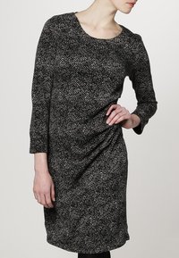 Robe à motifs noir et blanc avec un col rond, des manches trois quarts et un détail drapé à la taille. Tissu doux et texturé.