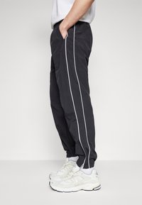 Zwarte broek van lichtgewicht materiaal, met witte zijkanten, een elastische tailleband en zijzakken. Gecombineerd met witte sneakers.
