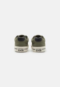 Zelena platnena tenisica s niskim profilom, s mornarsko plavim naglaskom na peti, bijelim gumiranim potplatom i crnim logom "Converse All Star" straga.