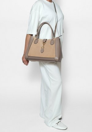 Sac à main beige et marron avec un design structuré, en cuir lisse, quincaillerie dorée, double poignées et détails de couture contrastés.