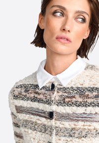 Cardigan strutturato con una combinazione di strisce crema, grigie e metalliche, dotato di un colletto bianco e bottoni neri per i dettagli.