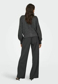 Hall nõelutud hall villane kampsun, millel on vaba lõige ja soonikserv, kombineeritud tumedashallide triibuliste wide-leg pükstega ja avatud varvastega mustade kontsadega kingadega.