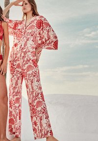 Un kaftan rouge et blanc à motif floral qui présente des manches larges, un décolleté en V et un pantalon ample, fabriqué en tissu léger.