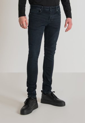 Jeans de mezclilla oscuros de corte ajustado con una textura suave. Llevados con zapatillas negras de cordones, que cuentan con un diseño minimalista y una suela acolchada.