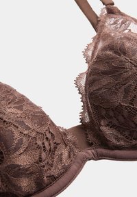 Sujeción de encaje marrón con diseño floral y tirantes ajustables, mostrado en primer plano sobre un fondo claro.