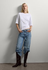 Top bianco oversize con maniche corte, jeans azzurri rilassati con risvolti, e stivali alti fino al ginocchio in vinile borgogna. Design semplice e casual.