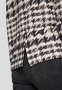 Schwarz-weiß gemusteter Hahnentrittstoff mit strukturierter Oberfläche, versehen mit einem seitlichen Schlitz. Kombiniert mit dunkelgrauem Denim, der eine klassische Gesäßtasche besitzt.