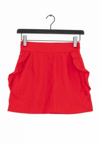 Rode mini rok met een gladde textuur, ruches aan de zijkanten en een afgewerkte zoom. Hangt aan een zwarte metalen hanger.