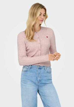 Cardigan en tricot de couleur rose clair avec un col rond, des manches longues et un petit détail en forme de cœur rouge sur la poitrine, fermeture par boutons et bords côtelés.