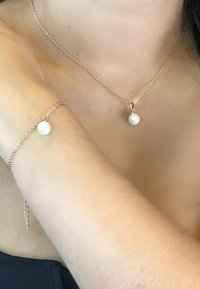 Collana e bracciale in oro rosa caratterizzati da un pendente rotondo in perla bianca, design con catena delicata, texture liscia e stile minimalista.