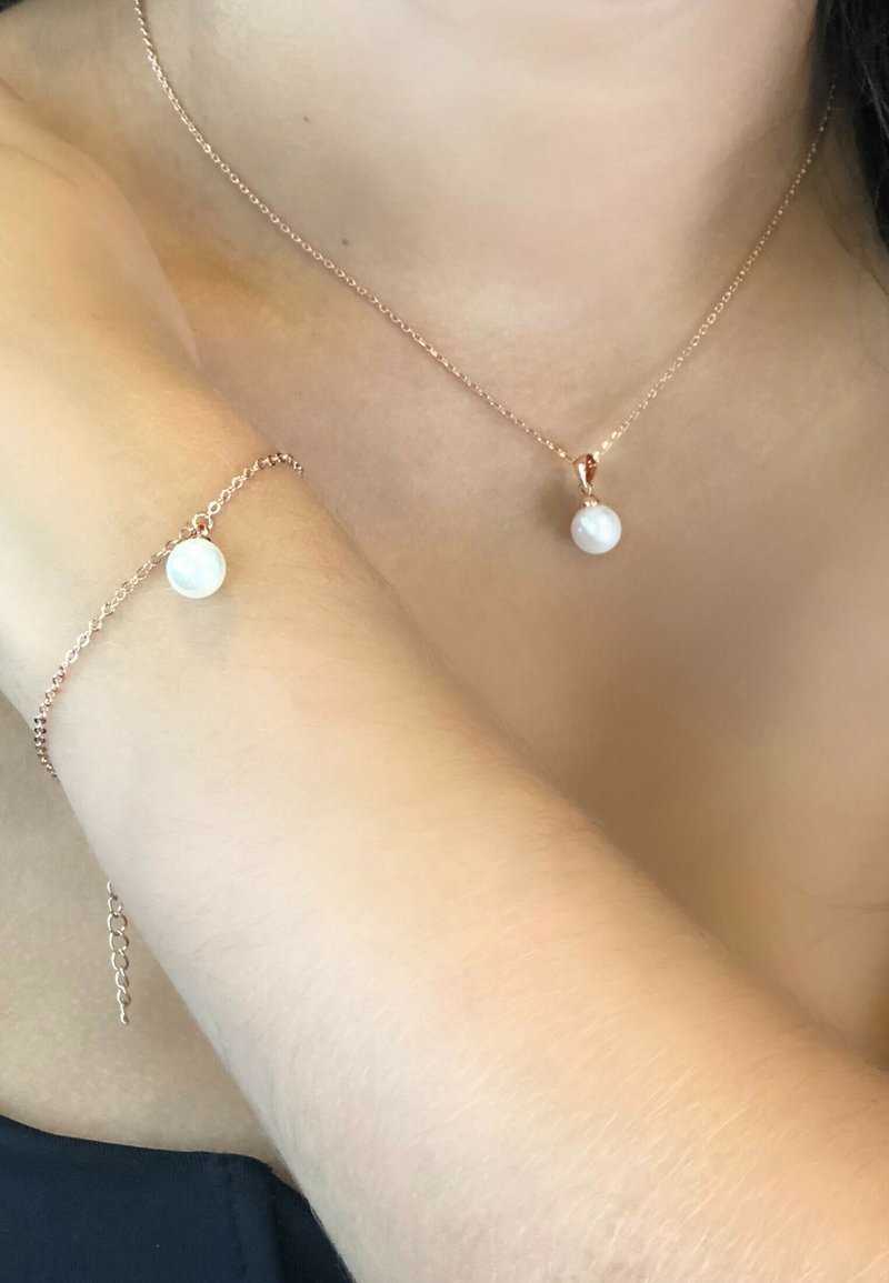 Collana e bracciale in oro rosa caratterizzati da un pendente rotondo in perla bianca, design con catena delicata, texture liscia e stile minimalista.