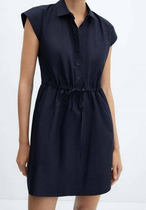 Frau trägt ein kurzärmeliges, marineblaues Kleid mit durchgehender Knopfleiste, Brusttasche und einem Taillenzug.