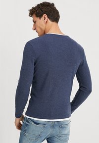 Granatowa koszula z długim rękawem wykonana z miękkiej tkaniny, z okrągłym dekoltem i dopasowanym krojem. Widoczne szwy i gładka struktura.