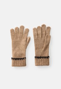 Et par beige strikkede handsker med sorte zigzag-kanter på ribbede manchetter, lagt fladt på hvid baggrund.