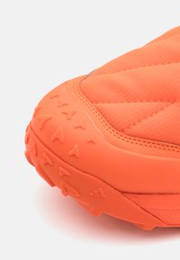 Shoe sportiv portocalie cu o talpa din cauciuc texturat, având modele proeminente, material superior matlasat și detalii de cusătură întărită.