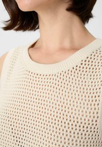 Light beige knitted top featuring a loose, open weave design, ribbed neckline, and textured fabric.