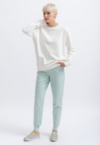 Felpa bianca con collo rotondo e orlo a costine, abbinata a pantaloni jogger verde menta chiaro con vestibilità affusolata e tasche laterali. Sneakers chiare.