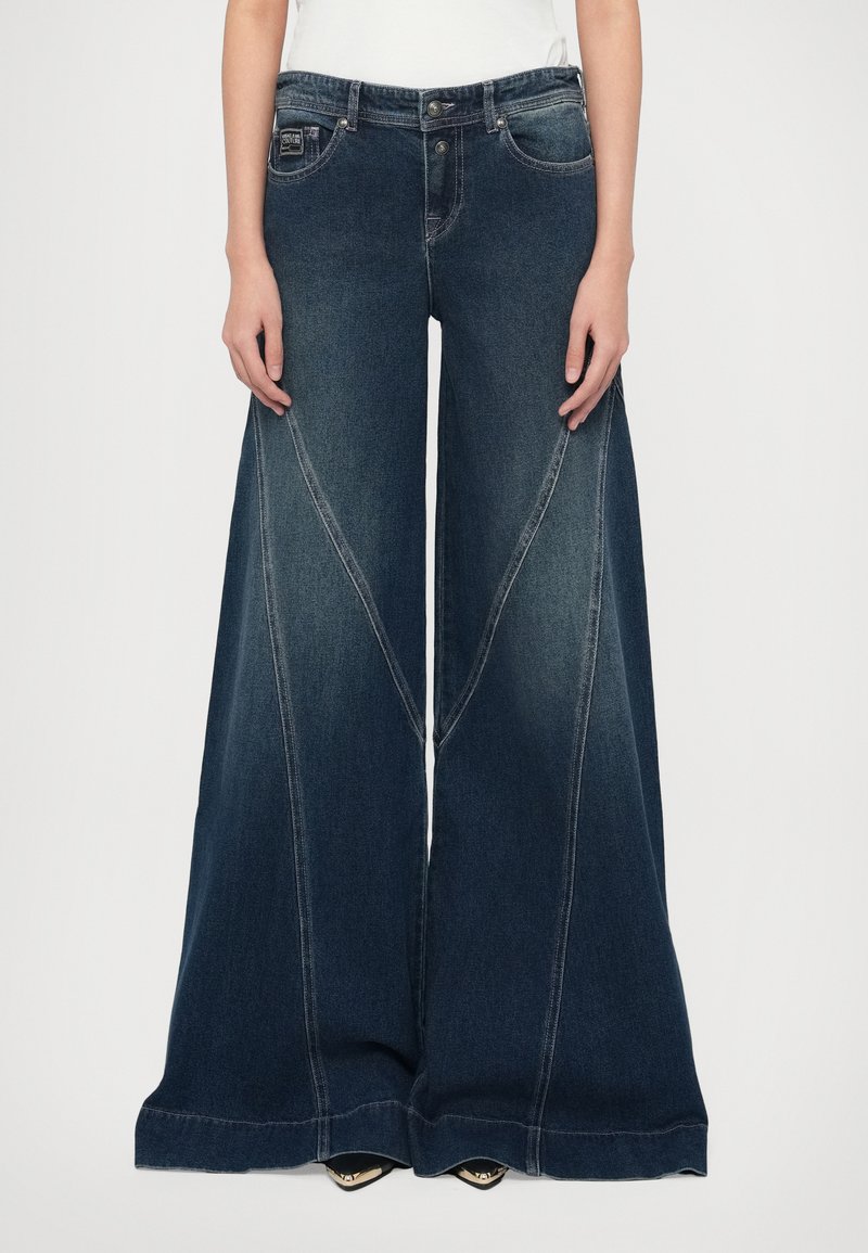 Široké džínsy z denimu tmavomodrej farby. Majú kontrastné švy, vysoký pás a zvonovitý strih. Sú viditeľné dve predné vrecká.
