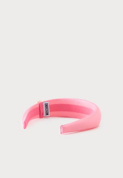 Bandeau en tissu rembourré rose avec une étiquette Moschino à l’intérieur, sur fond blanc uni.