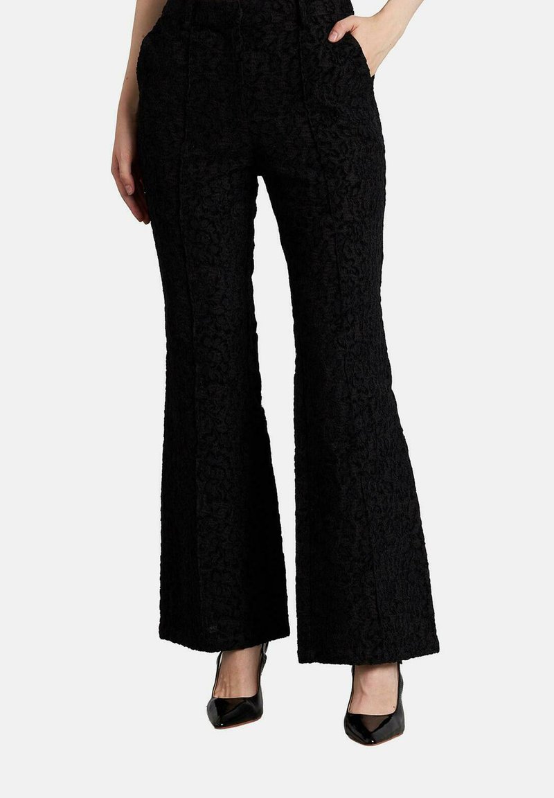Pantalones negros acampanados con un patrón floral texturizado, que presentan una cintura alta y dos bolsillos frontales. Combinados con tacones negros para un contraste.
