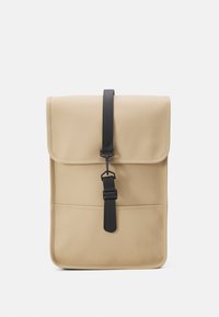 Sac fourre-tout beige avec un rabat, une bandoulière noire et une texture lisse. Présente une poche avant et un design minimaliste.