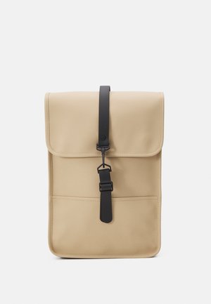 Beige schoudertas met een omslagflap, zwarte schouderriem en een gladde textuur. Heeft een voorkantvak en een minimalistisch ontwerp.
