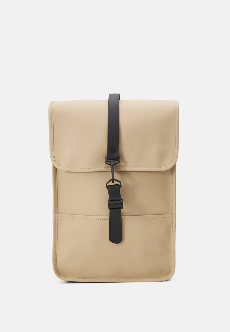 Sac fourre-tout beige avec un rabat, une bandoulière noire et une texture lisse. Présente une poche avant et un design minimaliste.