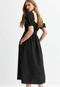 Vestido negro de longitud media con mangas abullonadas, fruncido elástico en la parte trasera y bolsillos laterales para mayor funcionalidad. Tejido suave y texturizado.