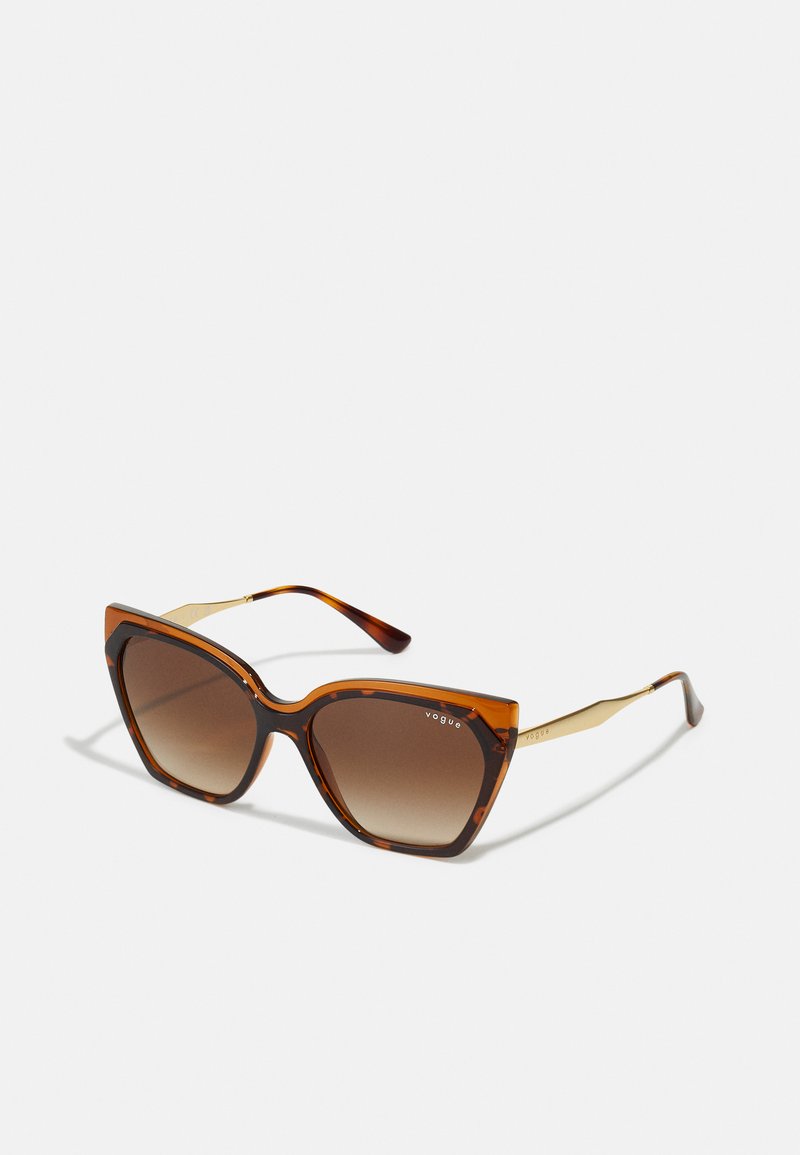 Lunettes de soleil en dégradé brun avec une forme œil de chat, monture à motif écaille de tortue et accents métalliques dorés sur les tempes.