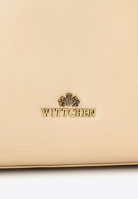 Jasnobeżowa skórzana torba z wytłoczonym na złoto logo "WITTCHEN" i misternymi motywami lwa nad tekstem. Gładka tekstura, minimalistyczny design.