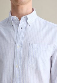 Camisa a rayas azul claro y blanca con cuello abotonado, un bolsillo en el pecho y cierre de botones. Fabricada con un tejido suave.