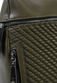 Textuur leren handtas in olijfgroen met een gewatteerd ontwerp, een ritssluiting en zilveren accenten. Zijvak met ritsdetails.