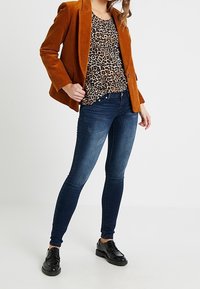 Oranžový kordurový sako přes leopardí top, zkombinované s tmavě modrými úzkými džíny a černými šněrovacími botami.