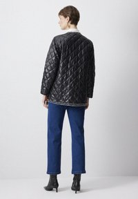 Black quilted jacket with a diamond pattern, featuring a white collar and decorative trim, paired with blue straight-leg jeans and black ankle boots.