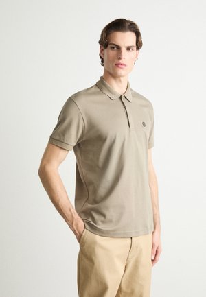 Beige Poloshirt mit Kragen, kurzen Ärmeln und einem kleinen Logo-Patch. Baumwollstoff mit glatter Textur und taillierter Passform.