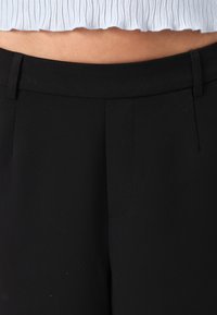 Svarte skreddersydde bukser med en glatt tekstur, med flat front og sidelommer. Designet for en tettsittende silhuett.