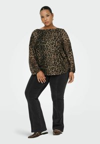 Blusa con stampa animale in tessuto trasparente con ampio scollo a barca, abbinata a jeans neri a campana. Le scarpe slip-on presentano un motivo coordinato.