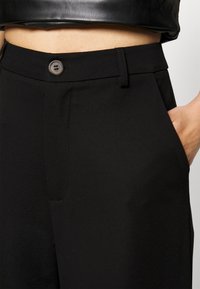 Svarta skräddarsydda byxor med en glatt tygkvalitet, med en framficka, knäppning med knapp och en figursydd midjedesign.